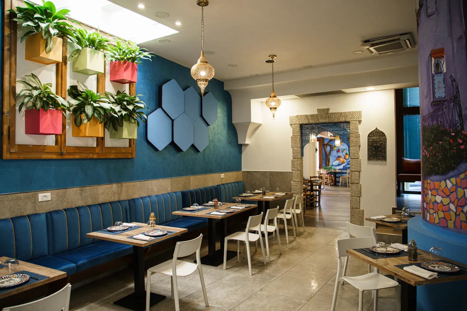 Sala ristorante con panche blu, piante e arco in pietra